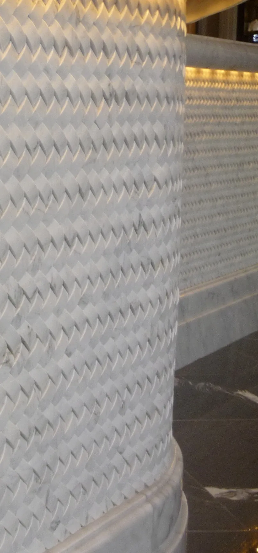 Superfície curva revestida a mármore branco, cada peça um paralelogramo chanfrado, montadas em espinha.