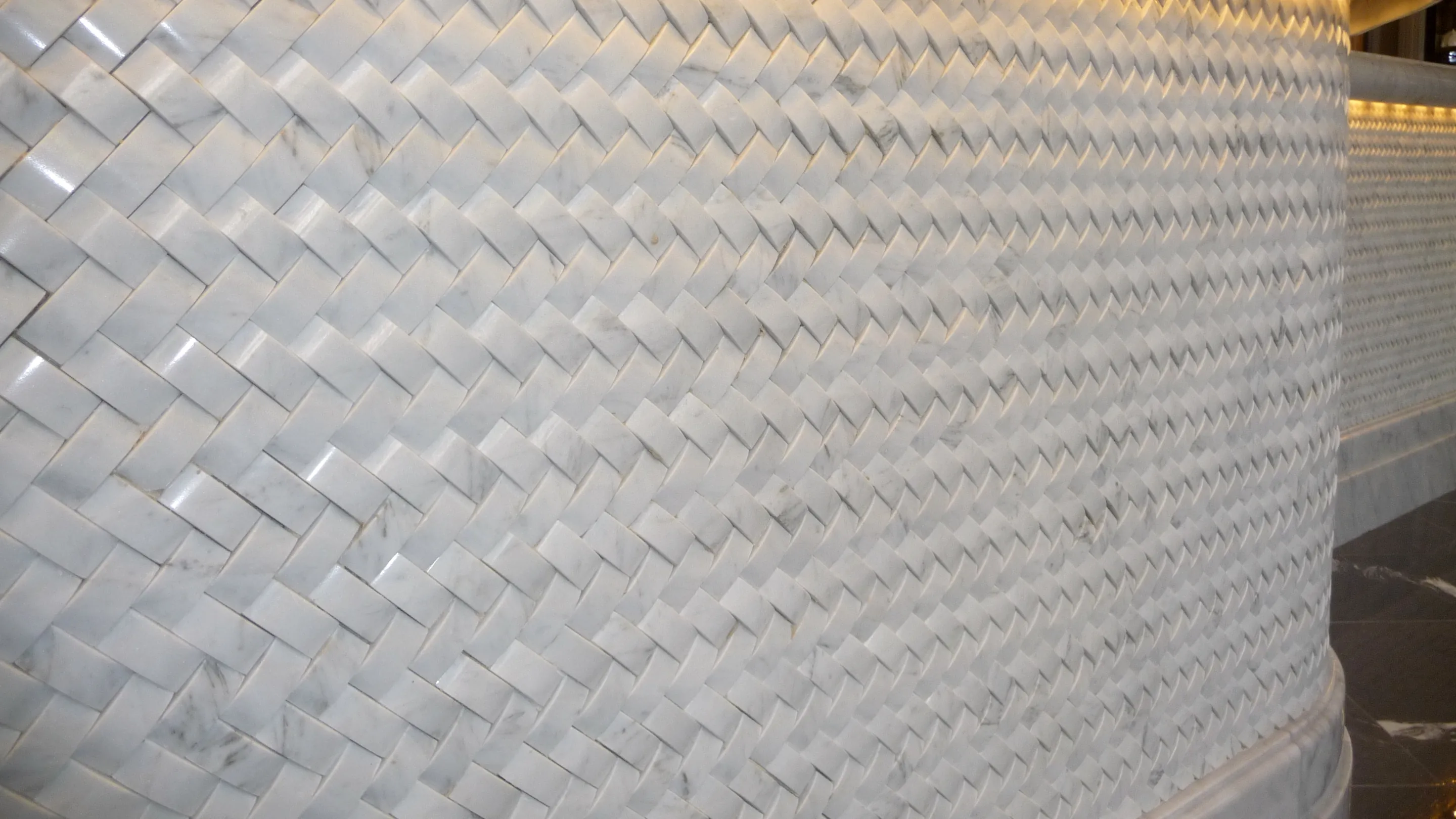 Superfície curva revestida a mármore branco, cada peça um paralelogramo chanfrado, montadas em espinha.